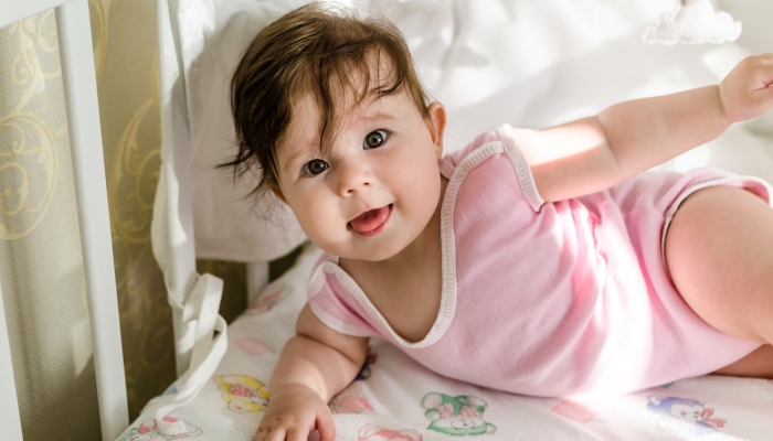 Cute sweet little baby girl having fun on her bed with a tongue out.
