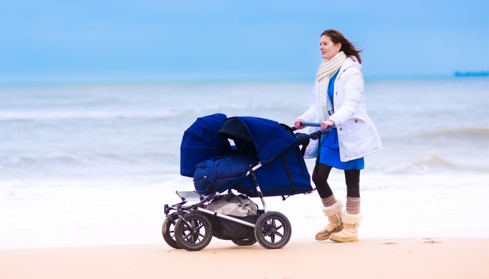 Happy active young mother walking on a beach pushing an all terrain double stroller with two kids.