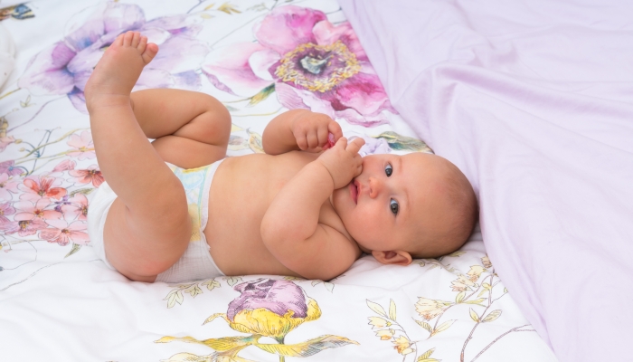 Happy little baby girl with a clean nappy after changing kicking her legs in the air as she lies on a bed.