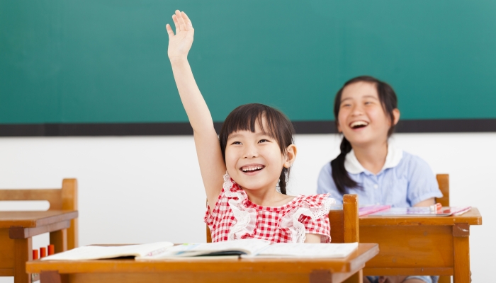 Happy school children raised hands in class.