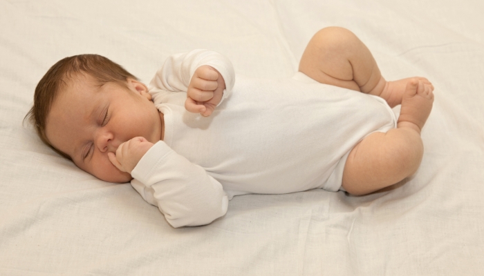Healthy newborn baby sleeping on white sheet.