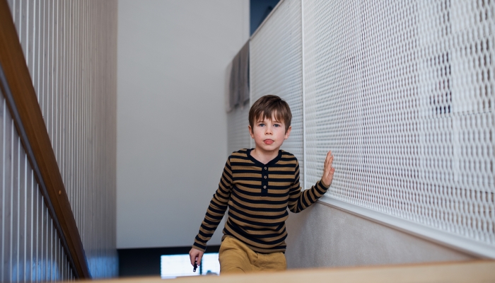 Little boy walking upstairs at home touching the wall.