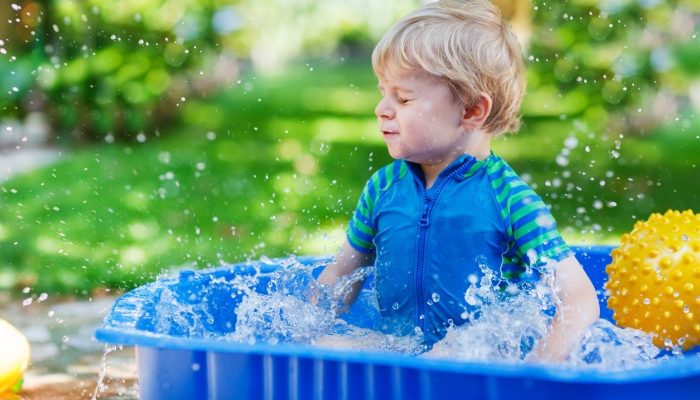 Little toddler boy having fun with splashing water in summer garden pool.