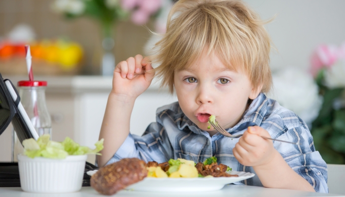 Little toddler child, blond boy, eating boiled vegetables, broccoli, potatoes and carrots with fried chicken meat at home.