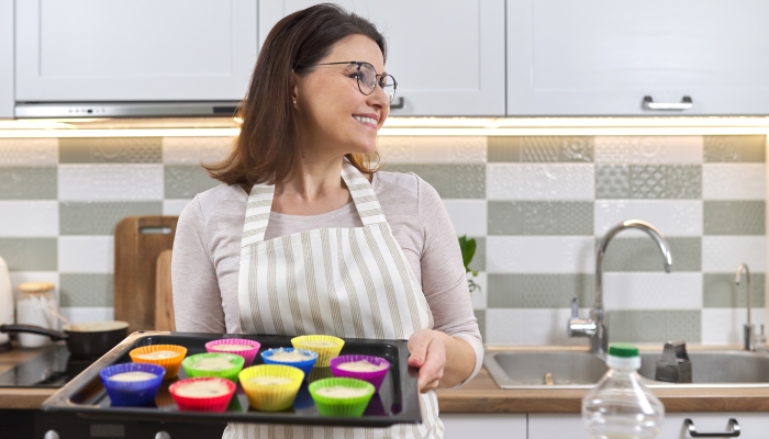 Mature woman in apron with baking tray with cupcakes being prepared.