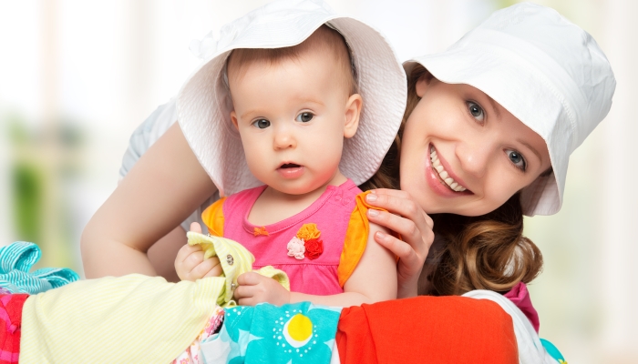 Mom and baby girl with suitcase baggage and clothes ready for traveling on vacation.