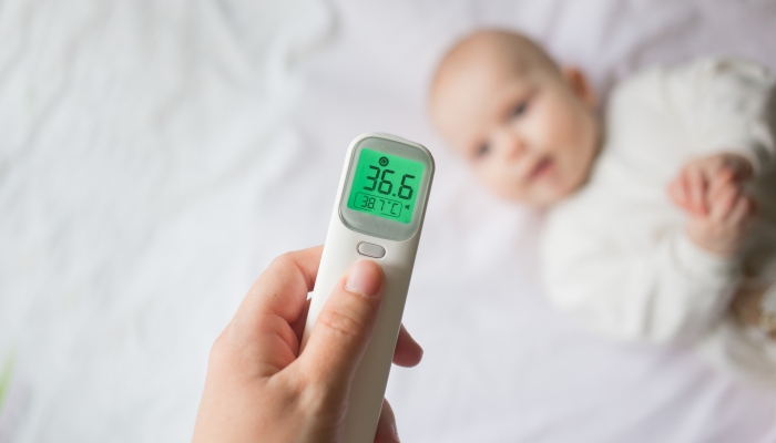 Mom's hand holds a thermometer at the child's forehead and measures his temperature.