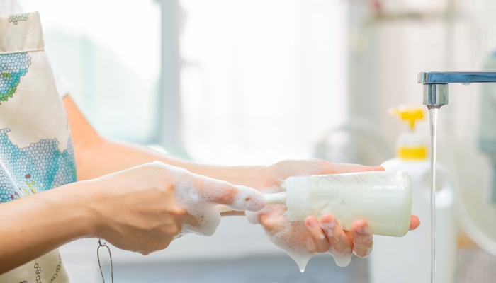 Mother cleaning baby milk bottles with bottle brush.