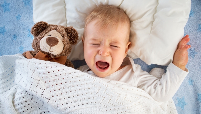 One year old baby crying in bed with a teddy bear due to nightmare.
