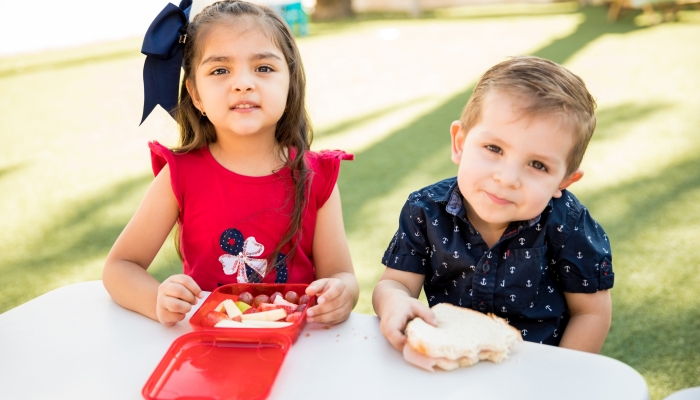 Portrait of a couple of kindergarten friends sitting together and eating snacks at school.