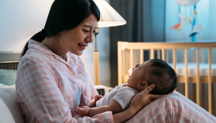 Portrait smiling asian new mom in pajamas is looking at her cute babbling.