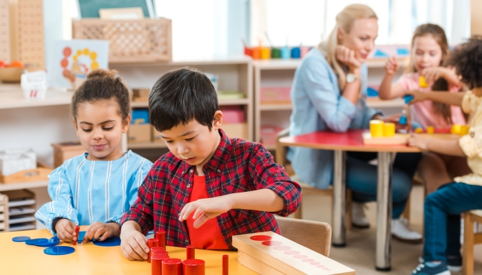 Selective focus of kids playing games with children and teacher at background in montessori school.