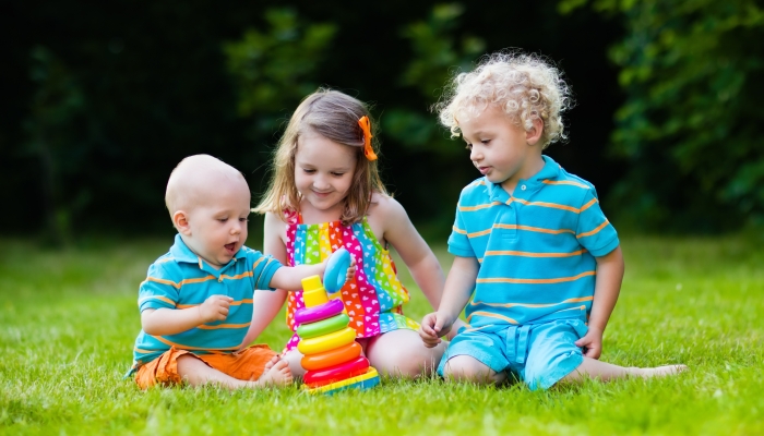 Three little children play with colorful rainbow pyramid toy.