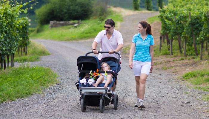 Young active parents hiking in the mountains with a double twin stroller with two children, brother and sister, baby boy and toddler girl