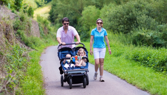 Young active parents hiking in the mountains with a double twin terrain stroller with two children.