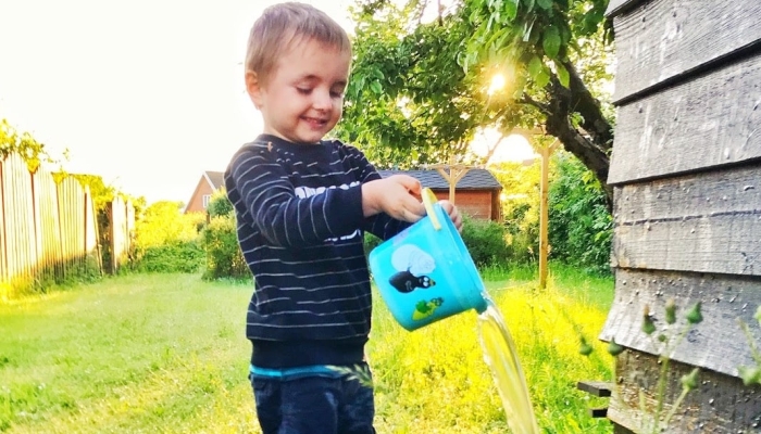 Toddler standing with hose and bucket.