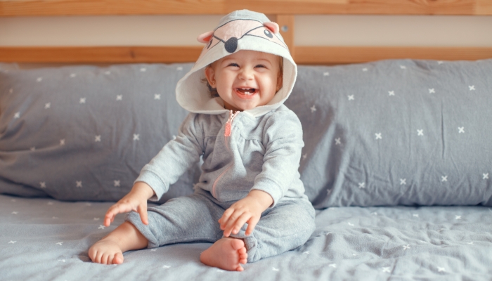 Adorable baby in grey pajama with fox cat animal hood sitting on bed in bedroom.