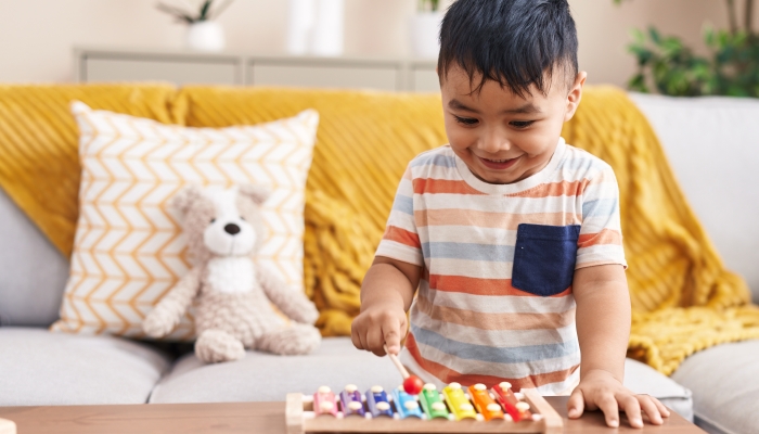 Adorable hispanic toddler playing xylophone standing at home.