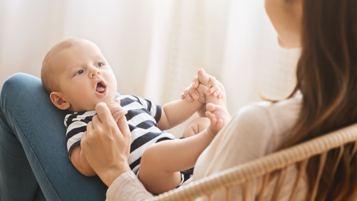 Adorable newborn baby cooing while lying on mother's lap, over shoulder shot, panorama.