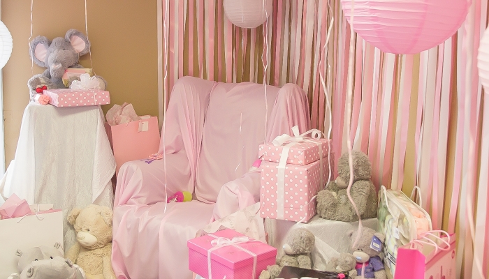 Baby shower chair with gifts and pink balloons and streamers and teddy bears.