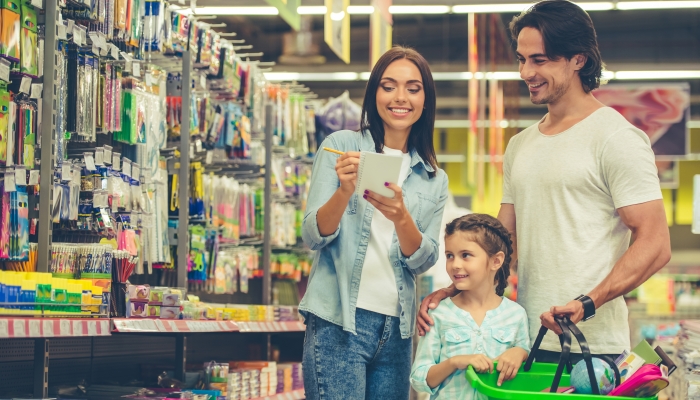 Beautiful young parents and their cute little daughter are smiling while choosing school stationery in the supermarket.