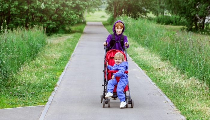 Boy pushing a big stroller for his brother.