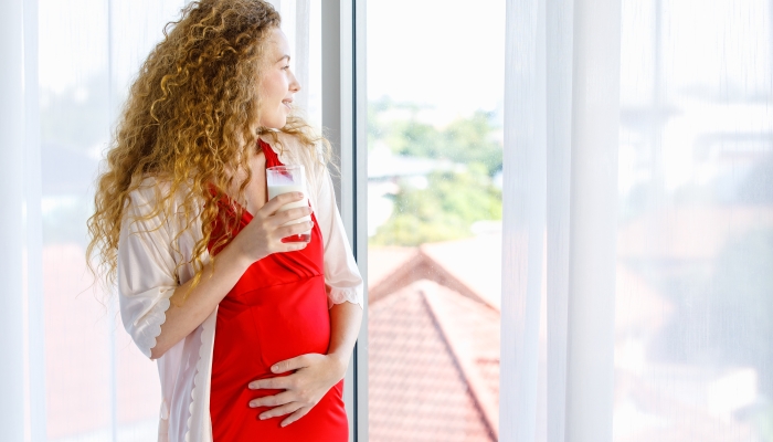 Caucasian curly long hairstyle pregnant female mother in red maternity dress pajama.