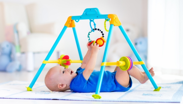 Cute baby boy on colorful playmat and gym, playing with hanging rattle toys.