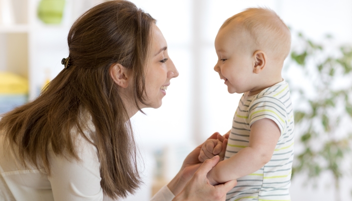 Cute little baby plays with his young mom in bedroom.