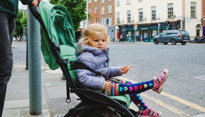 Cute little toddler girl sitting in baby stroller while walking with dad on the streets of big city.