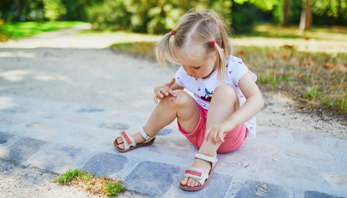 Cute little toddler girl sitting on the ground after falling at summer park.