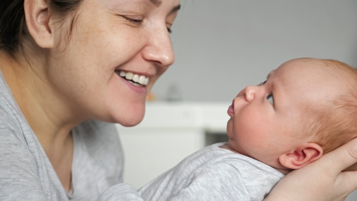 Happy mother babbles with newborn baby girl holding in arms.