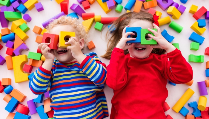 Happy preschool age children play with colorful plastic toy blocks.