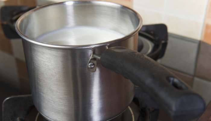 Milk in a saucepan on a gas stove burner.
