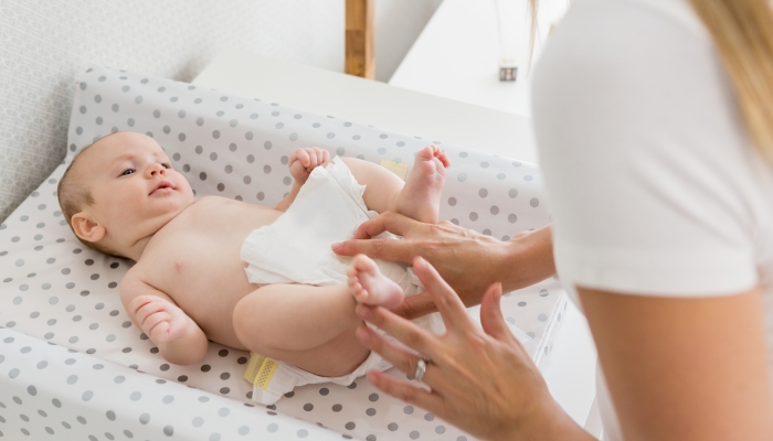 Mother changing the diaper of her baby at home.