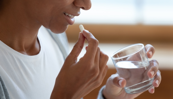 Smiling young African American woman take daily dose of vitamin after pregnancy.