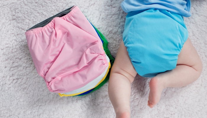 The child lies near a stack of multi-colored reusable clothe diapers on a changing table.