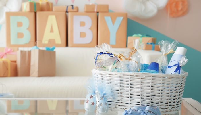 Wicker basket with gifts for baby shower party on table indoors.