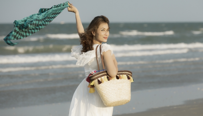 Woman carry big handcraft bag walking on beach play with cloth in strong wind and walking on beach.