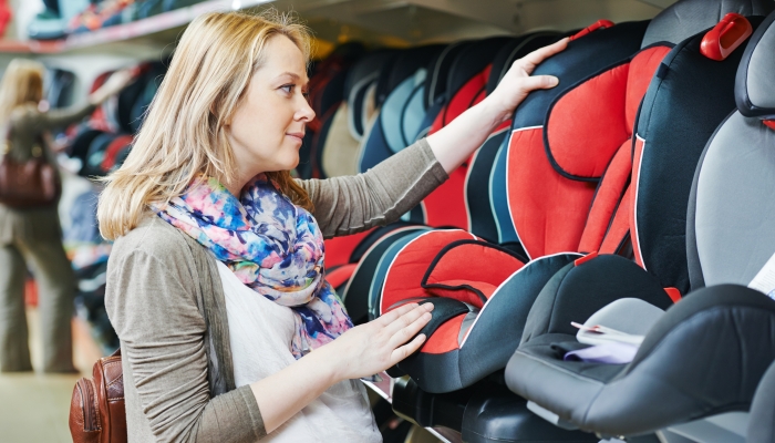 Woman choosing child car seat for her baby in shop supermarket.