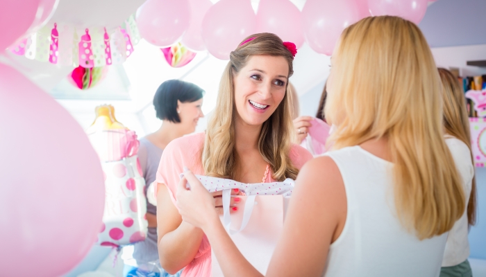 Woman giving gift to pregnant friend on baby shower party.