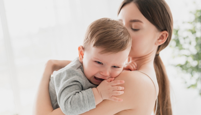 Young single mother cradling her crying daughter due to teething problem.