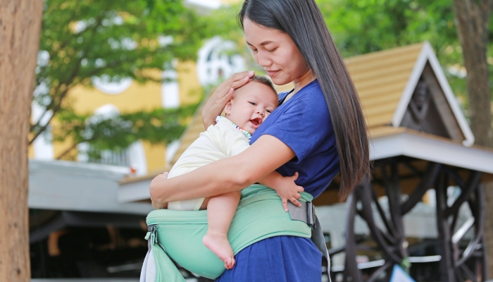 Asian mother hugging her infant on an ergonomic baby carrier.