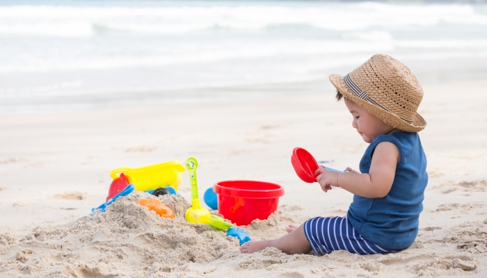 Asian one year old baby boy playing sand on the beach.