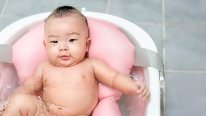 Asianmother give a bath newborn baby in a tiny bathtub in bathroom.