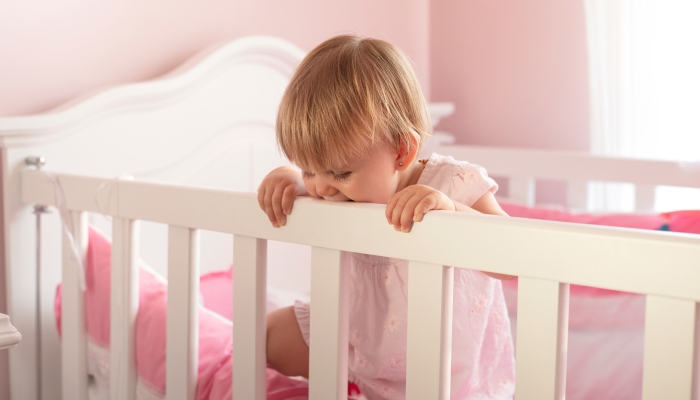 Baby girl standing in wooden crib.