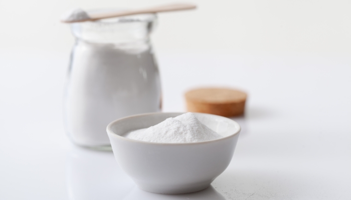 Baking soda in a jar and bowl on a white glossy background.