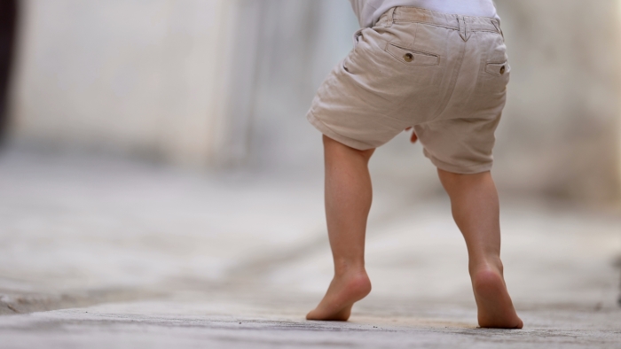 Child walking on tiptoes outside.