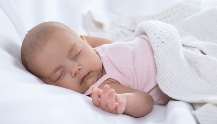 Cute little baby in bodysuit sleeping on bed.