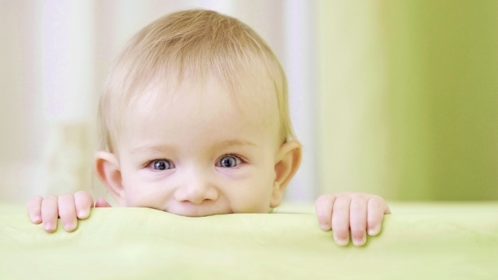 Happy baby portrait in crib, smiling face, child climbing with hands.